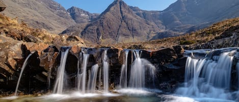 Una cascada fluye sobre rocas con una montaña al fondo.