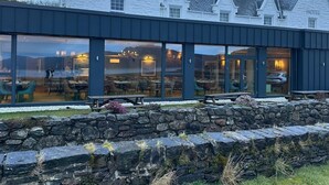 A hotel with a white exterior, stone wall in front, and large windows. - Balmacara Hotel (Kyle)