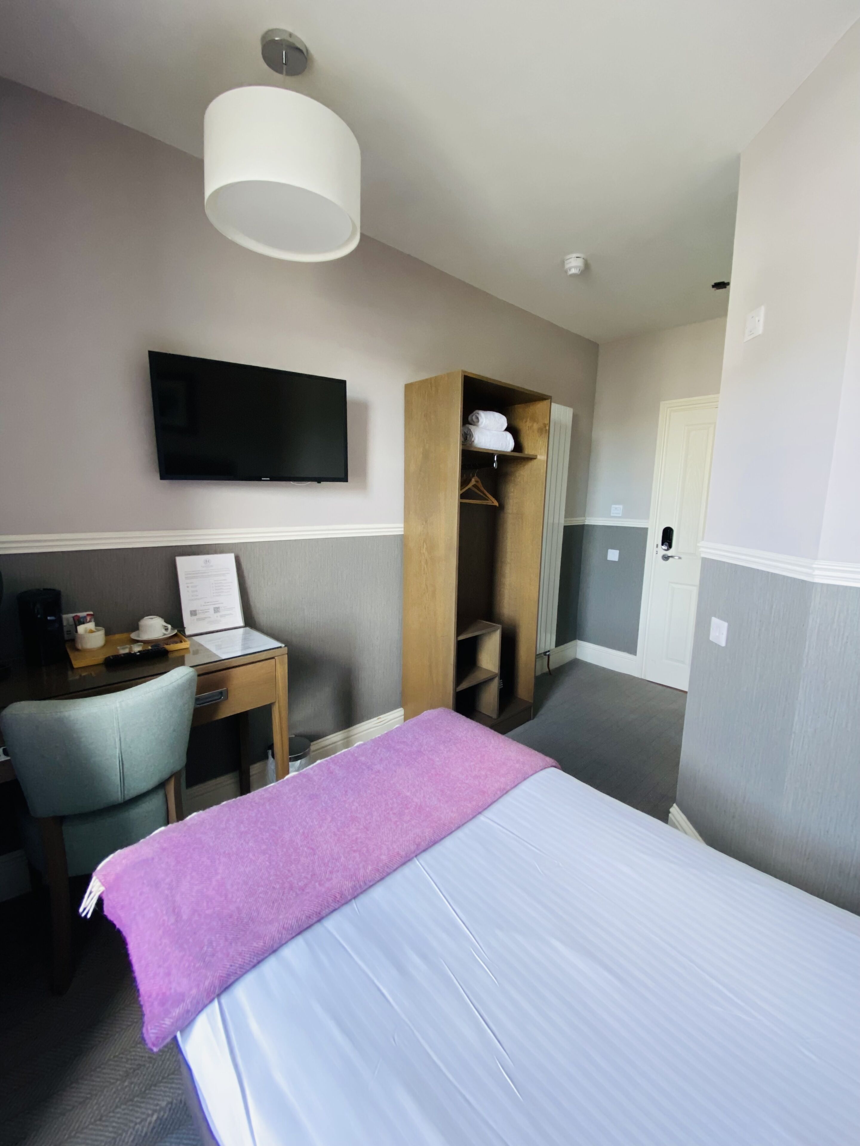 Une chambre d’hôtel équipée d’un lit, d’un bureau, d’une chaise, d’un téléviseur fixé au mur et d’une armoire.