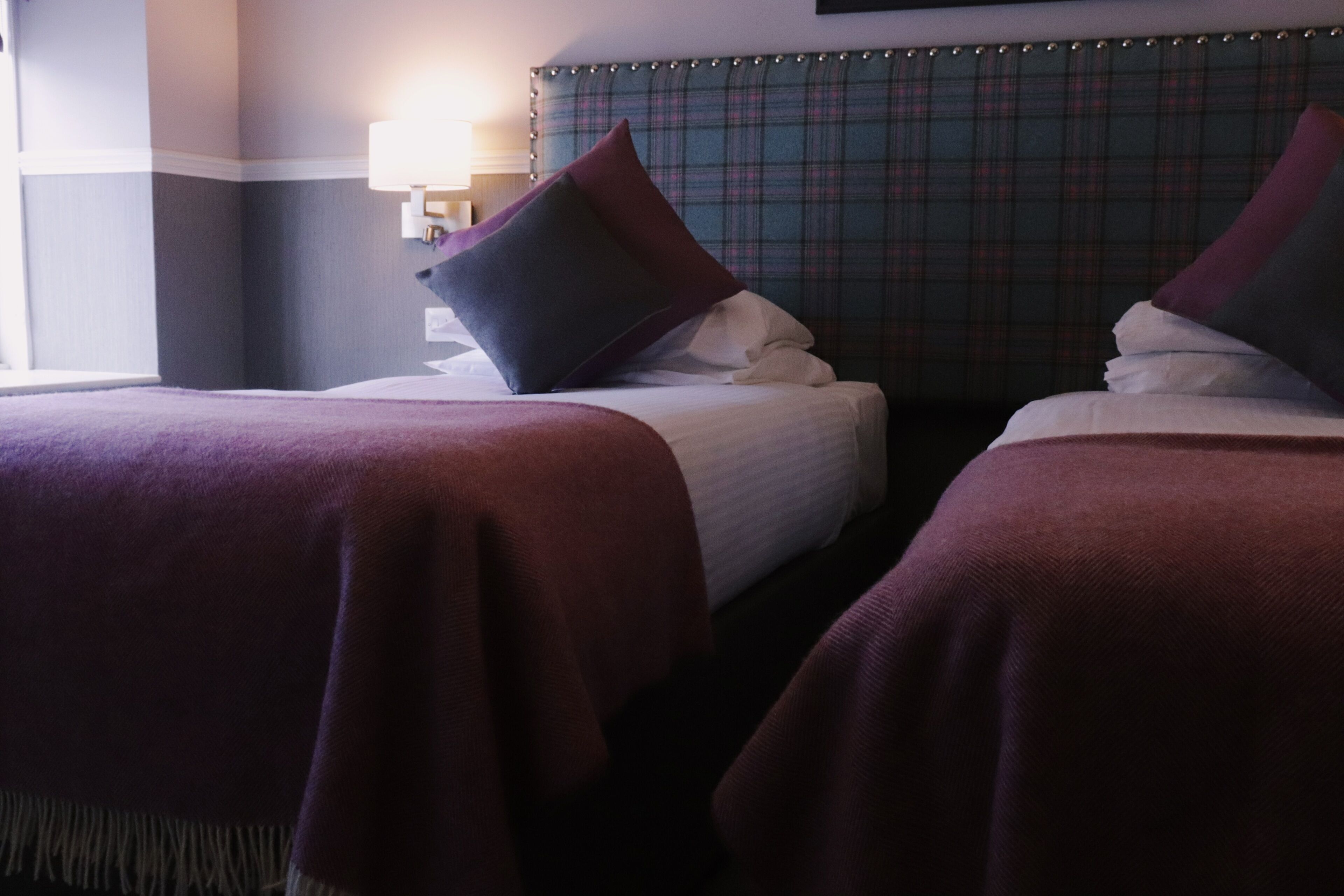 Hotellihuone, jossa on kaksi sänkyä, ruutukuviollinen pääty ja yöpöytälamppu.
