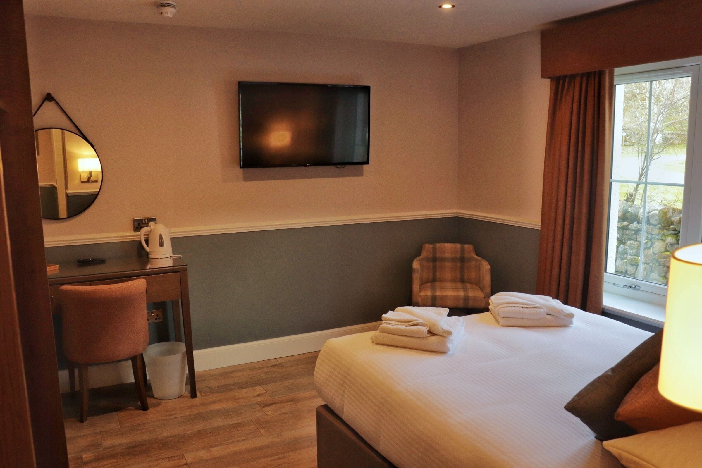 Habitación de hotel con cama, escritorio, silla, televisor y ventana con cortinas.