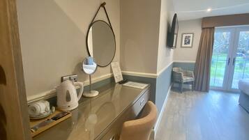 A hotel room with a desk, a mirror, a kettle, and a chair.