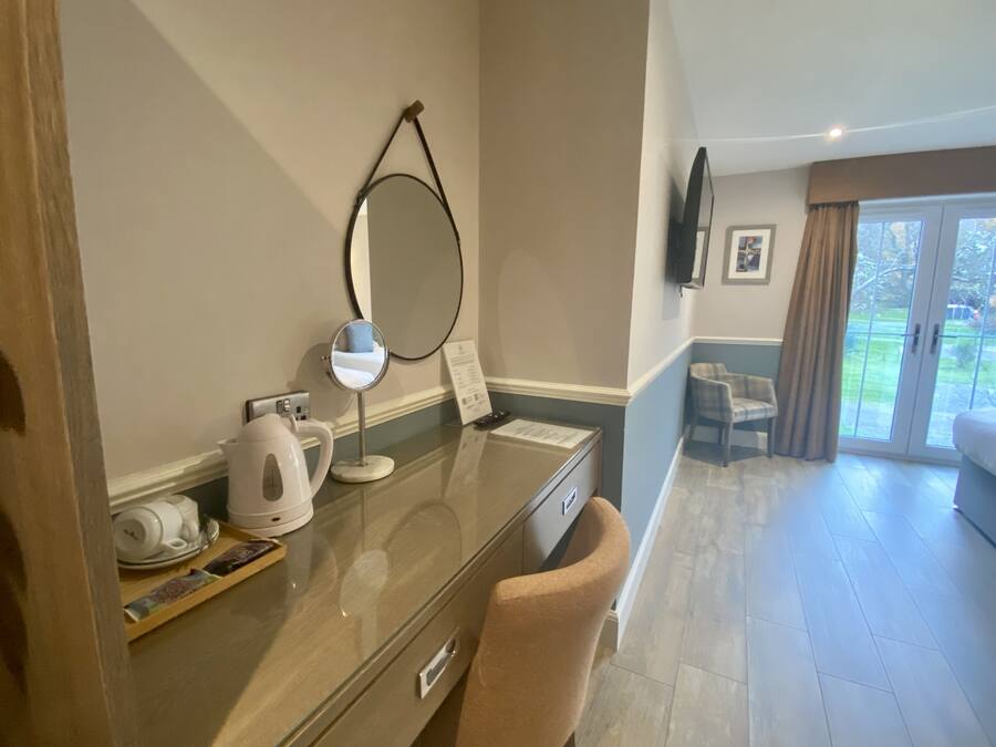 A hotel room with a desk, a mirror, a kettle, and a chair.