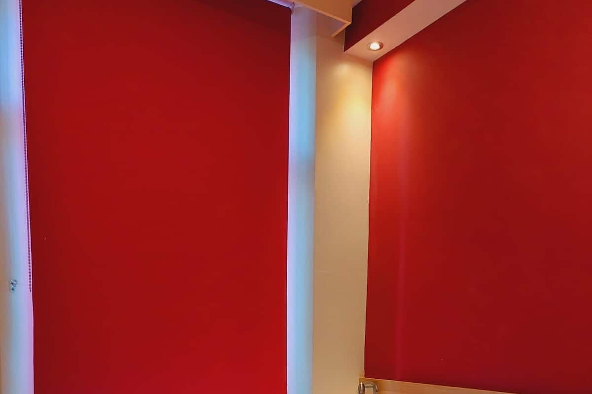Habitación de hotel con cama, cortinas rojas, colcha a cuadros y cabecero de madera.