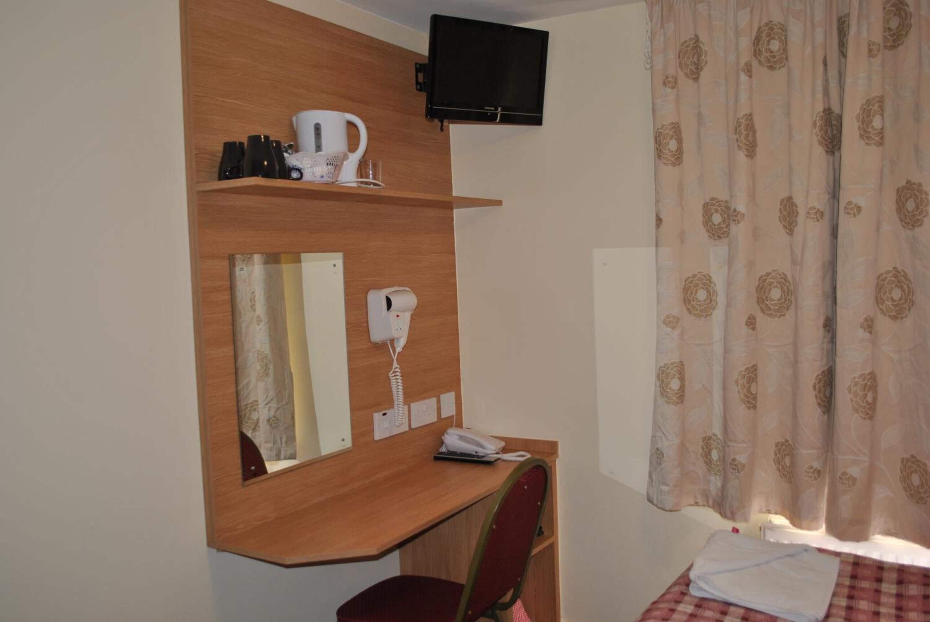 Ett hotellrum med ett skrivbord i trä, en hårtork, en telefon och en tv som är monterad ovanför skrivbordet, samt en säng med ett rutigt överkast.