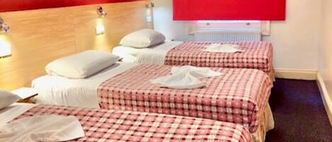 A hotel room with three beds, each with a red and white checkered bedspread, white pillows, and a red curtain.