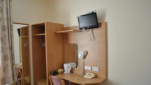 Una habitación de hotel funcional con un escritorio de madera, un televisor montado en la pared, un teléfono y un espejo.