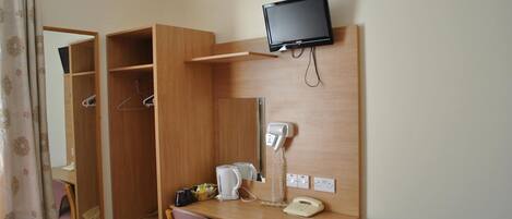 A compact hotel room with a wooden desk, a television mounted on the wall, a telephone, and a mirror.
