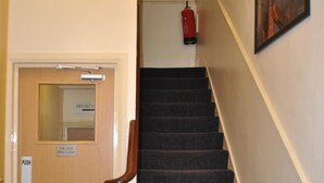 Una escalera con barandilla, un extintor instalado en la pared y una puerta con un letrero que indica que es una puerta cortafuegos.