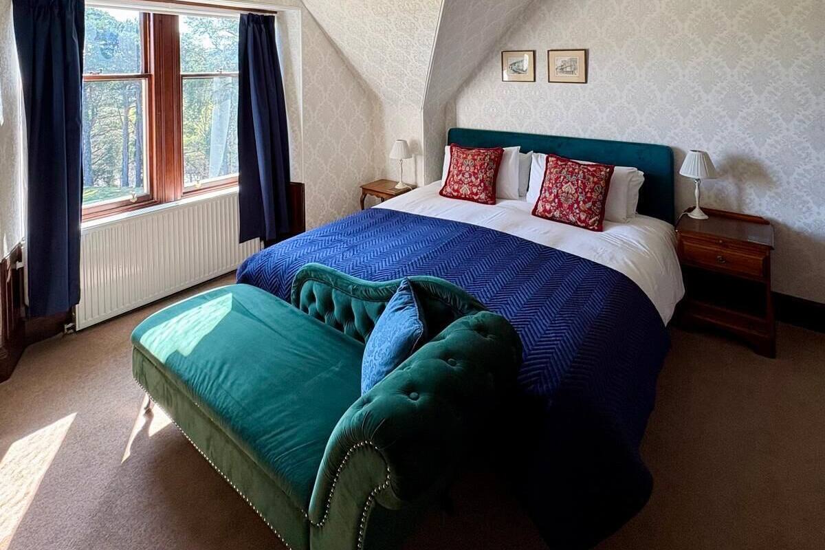 Een slaapkamer met een groot bed, een nachtkastje, een raam met gordijnen en een plafondlamp.
