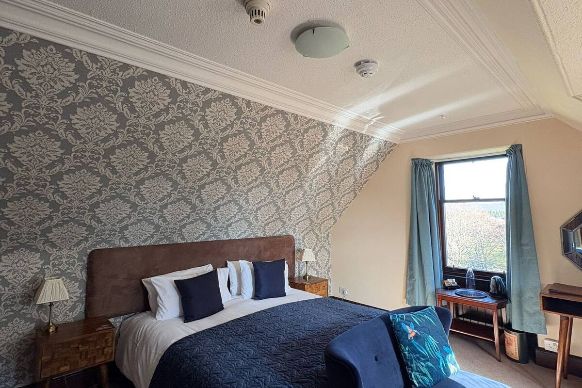 Een slaapkamer met een groot bed, een stoel, een bureau en een raam met gordijnen.