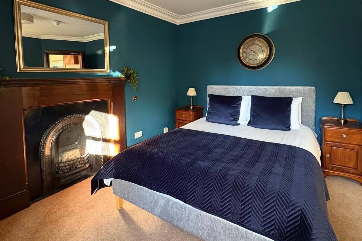 Een slaapkamer met een groot bed, een open haard, een spiegel en een klok aan de muur.