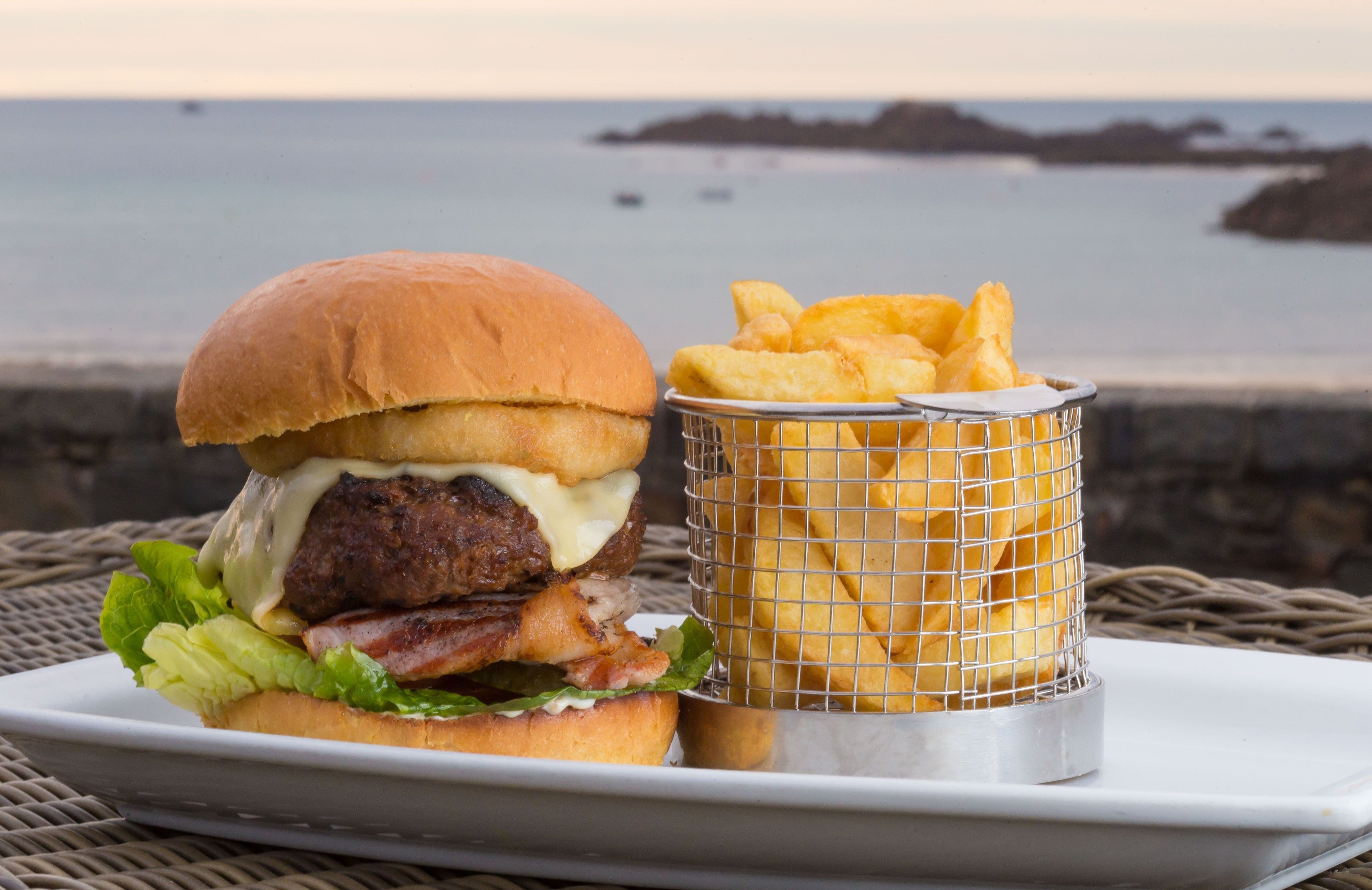 A burger with fries on a tray by the sea.