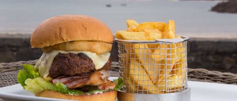 A burger with fries on a tray by the sea.