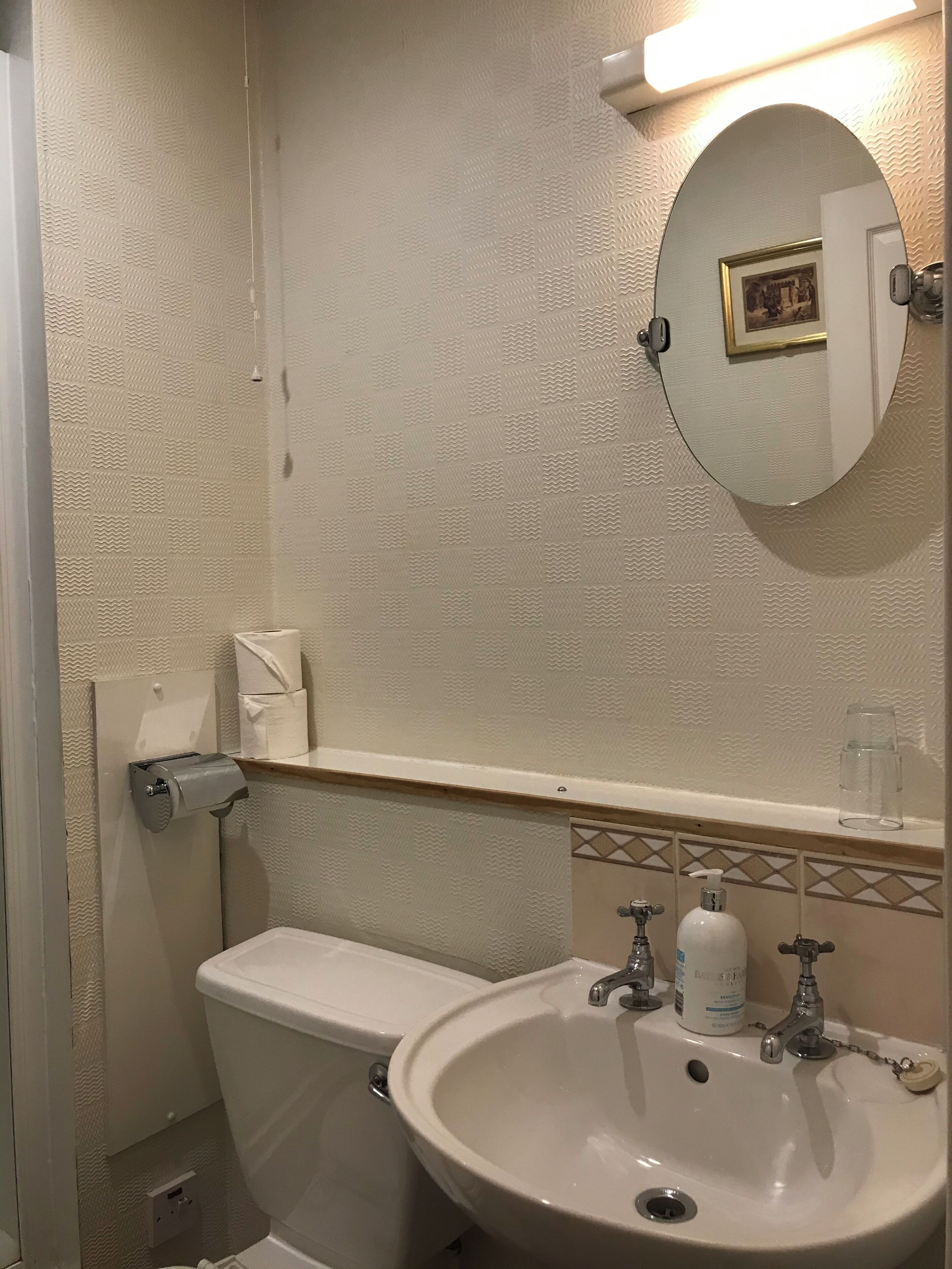 Une salle de bain équipée d’un WC, d’un lavabo, d’un miroir et d’un distributeur de serviettes.