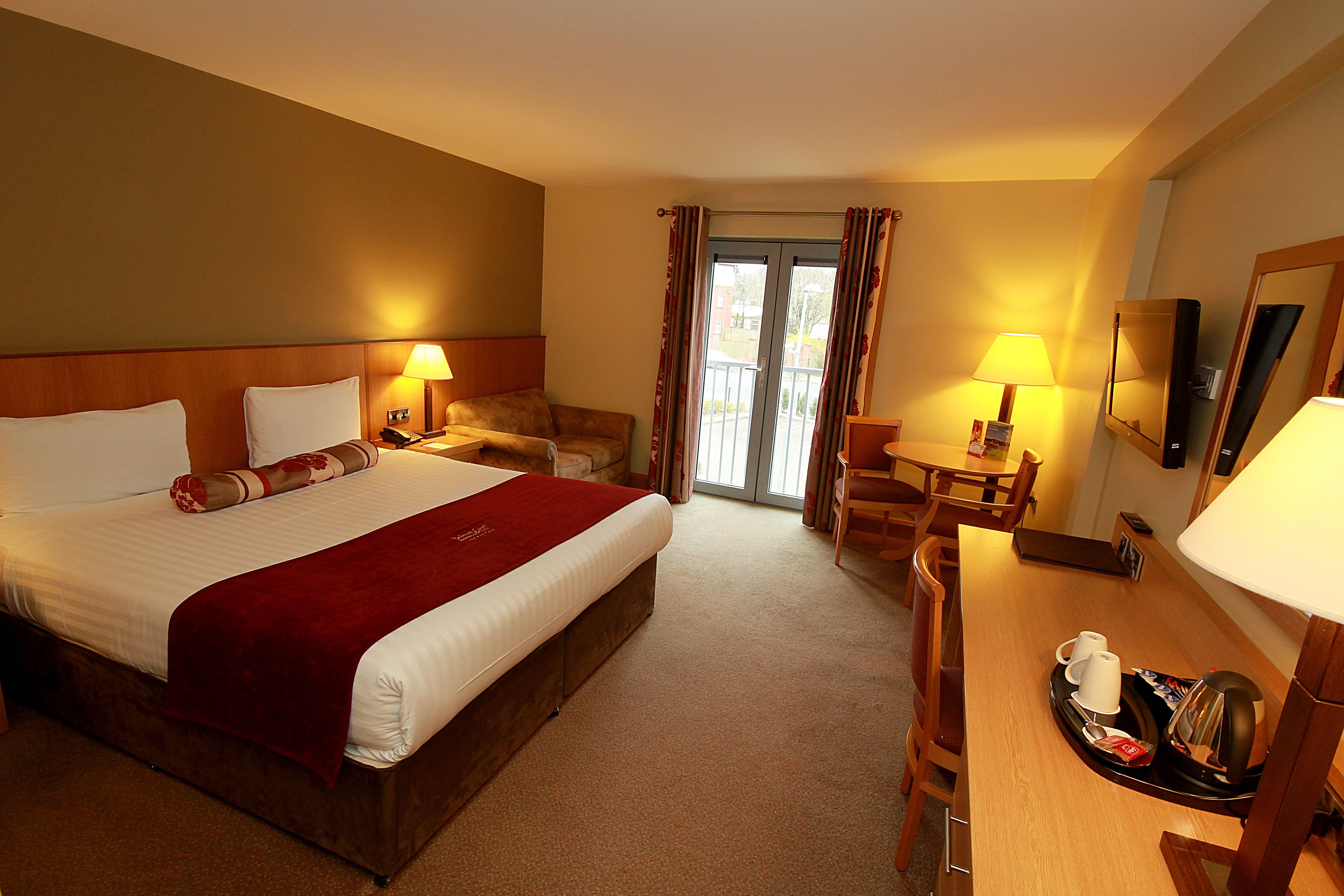 A hotel room with a large bed, a desk, a chair, a dining table, and a balcony with curtains.