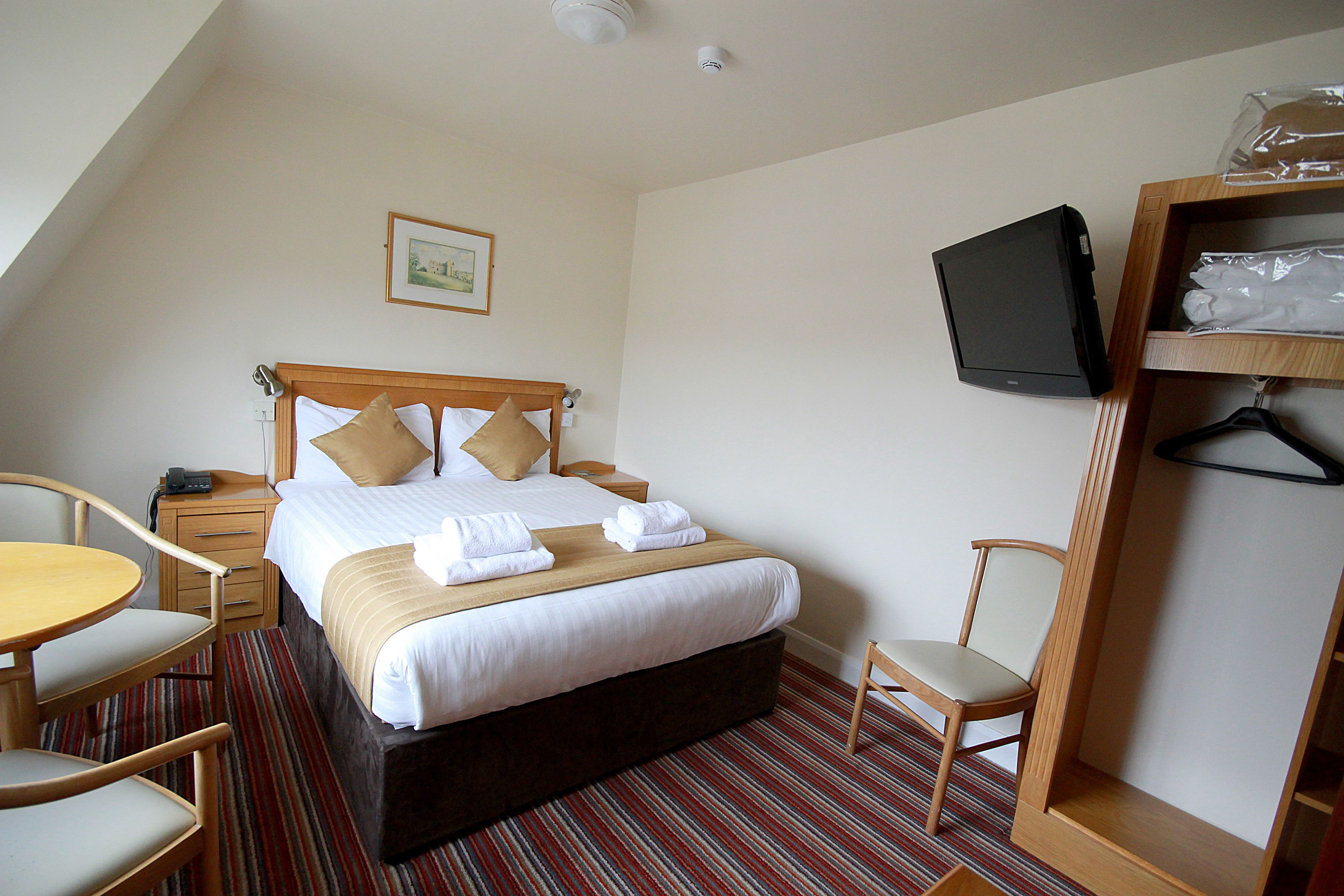 A hotel room with a bed, a television, a desk, a chair, and a wardrobe.