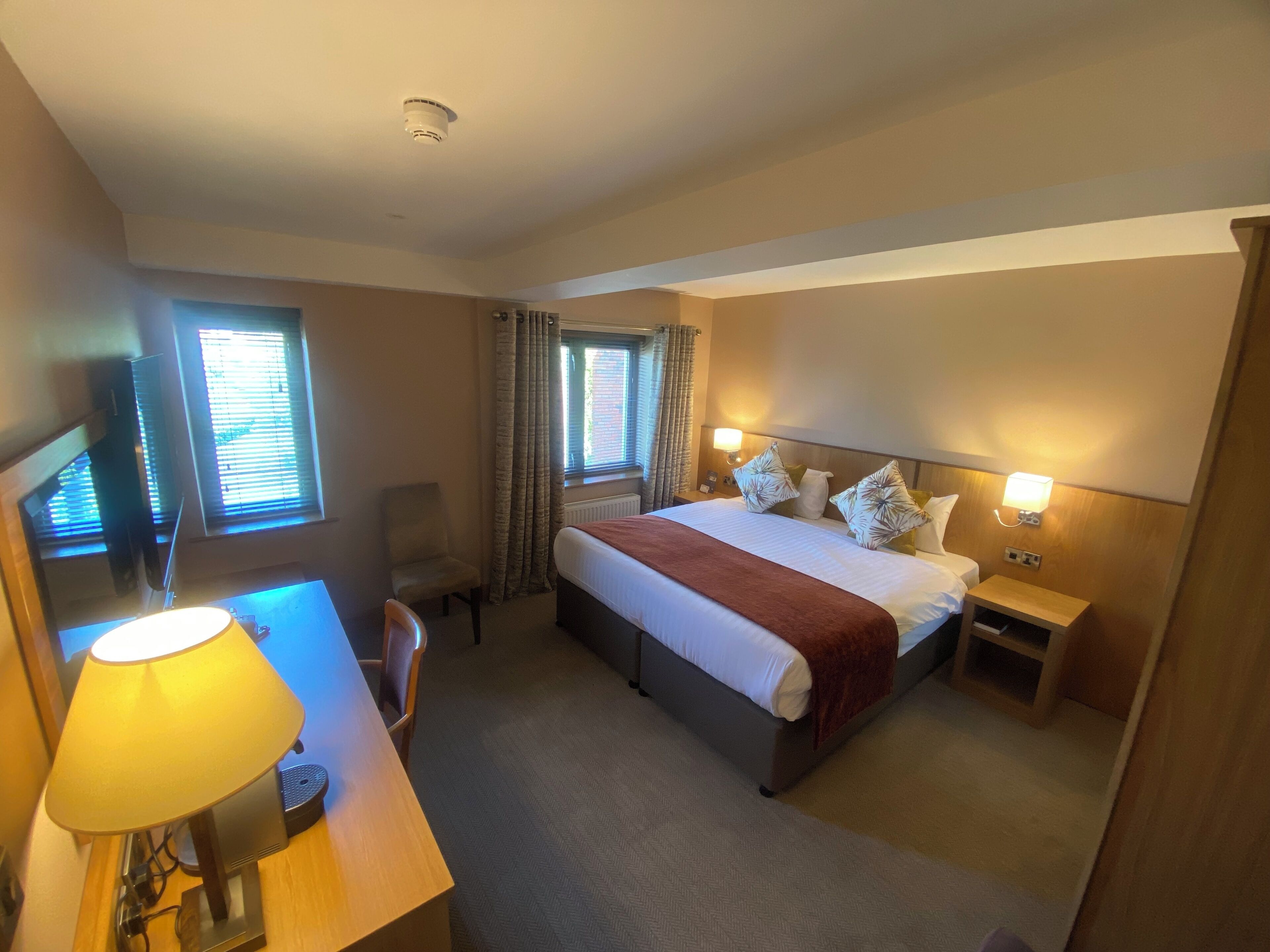 Habitación de hotel con cama, mesitas de noche, un escritorio con lámpara, una silla y televisor.
