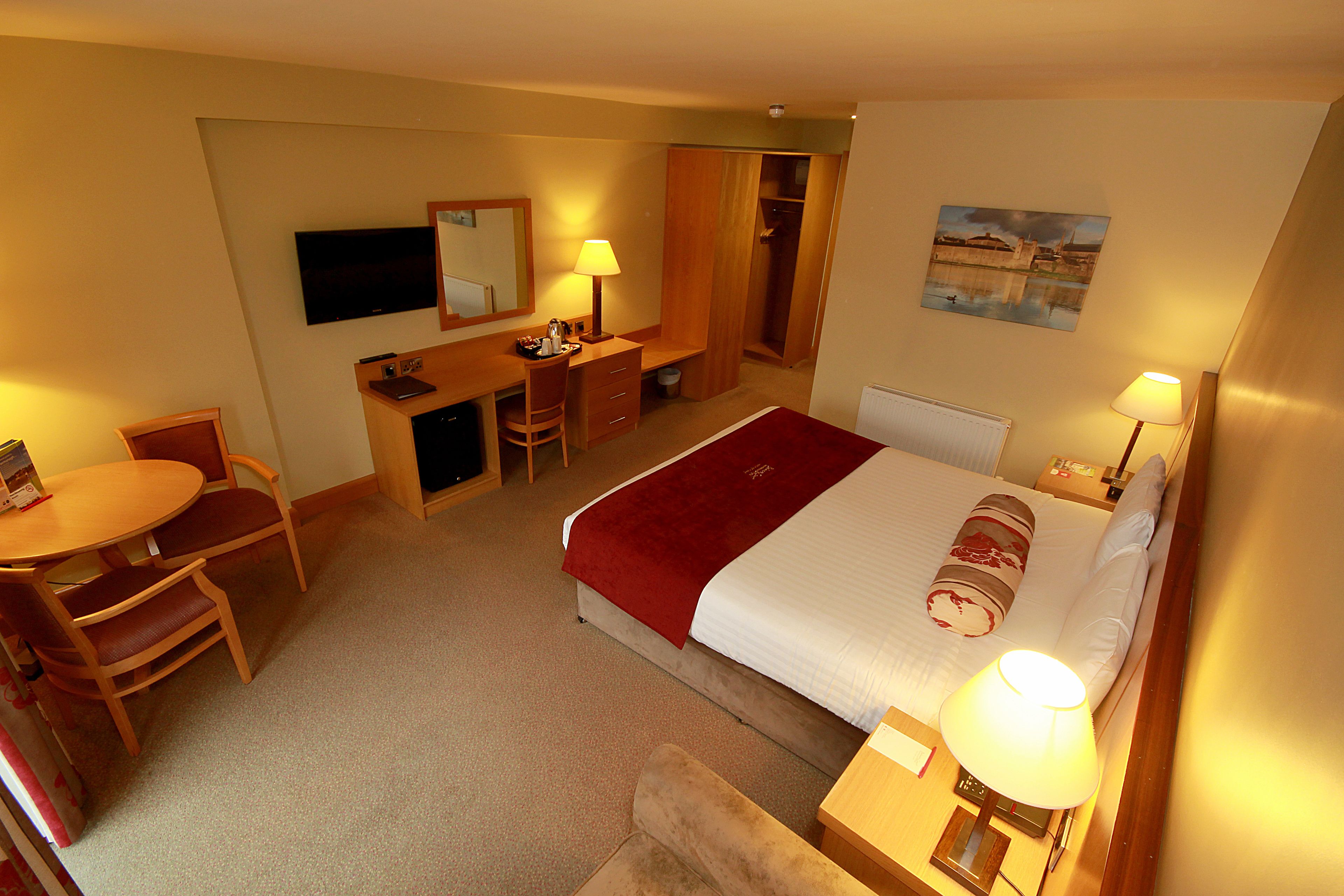 A hotel room with a bed, desk, chair, and a television.