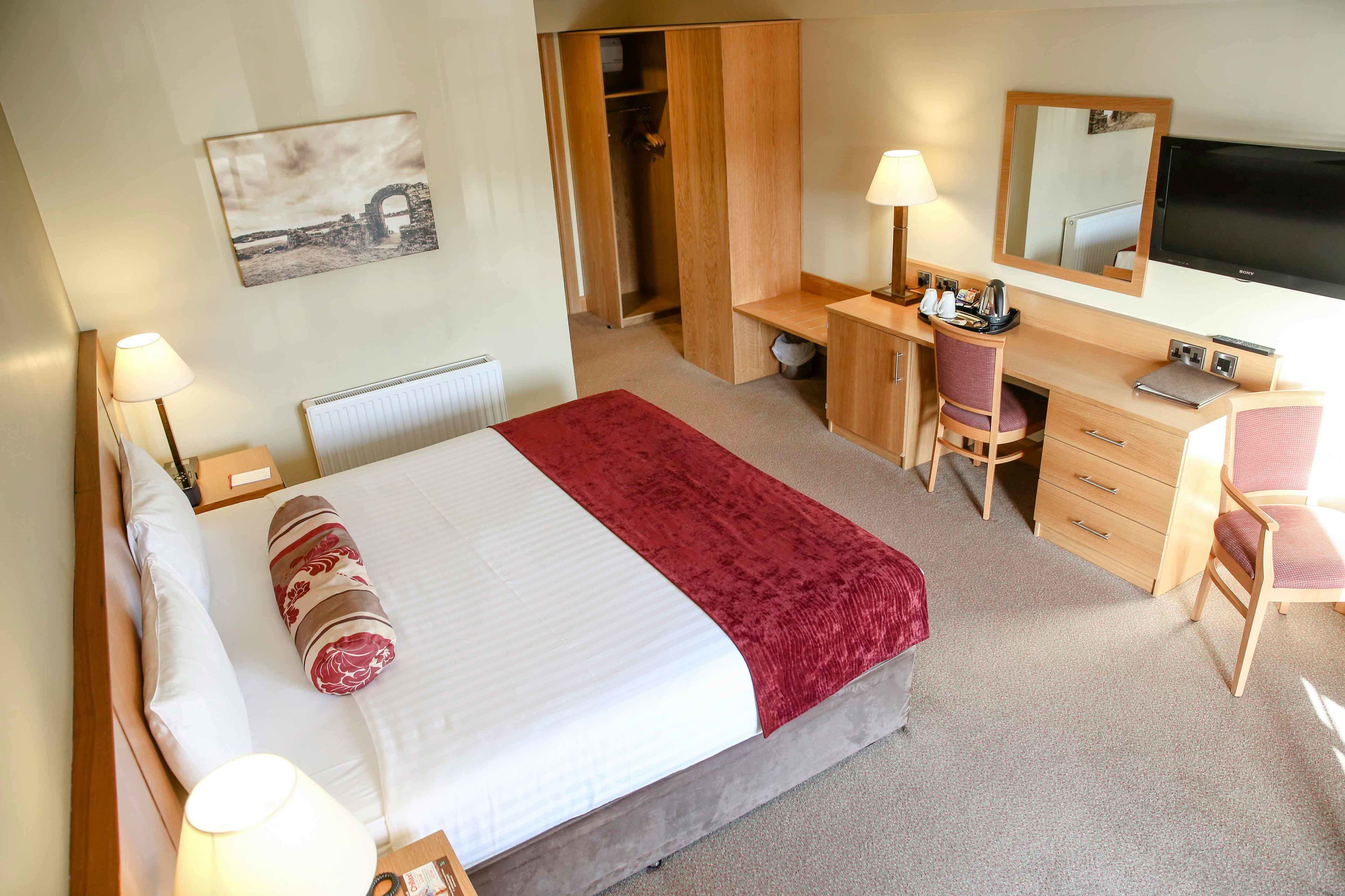 A hotel room with a bed, a desk, a chair, a wardrobe, a TV, and a lamp.