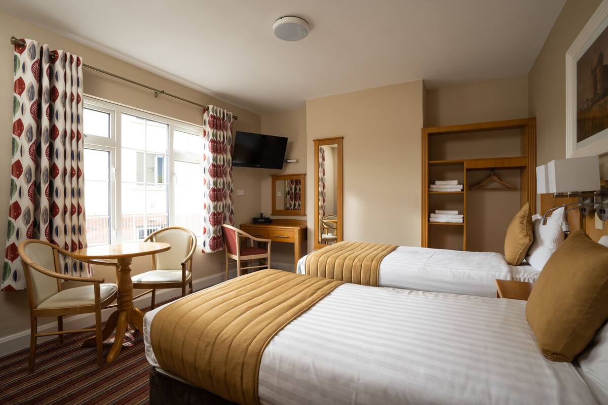 Ein Hotelzimmer mit zwei Betten, einem Schreibtisch, einem Sessel, einem Fernseher und einem Kleiderschrank.