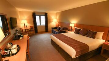 A hotel room with a large bed, two bedside tables, a desk with a chair, a television, and a window with curtains.