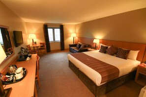 A hotel room with a large bed, two bedside tables, a desk with a chair, a television, and a window with curtains. - Belmore Court & Motel (Enniskillen)