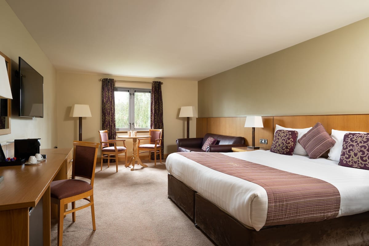 Ein Hotelzimmer mit einem großen Bett, einem Schreibtisch mit Stuhl, einem Fernseher und einem Fenster mit Vorhängen.