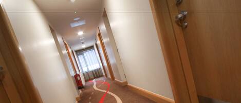En hotellkorridor med ett mattbeklätt golv, trädörrar och en brandsläckare.