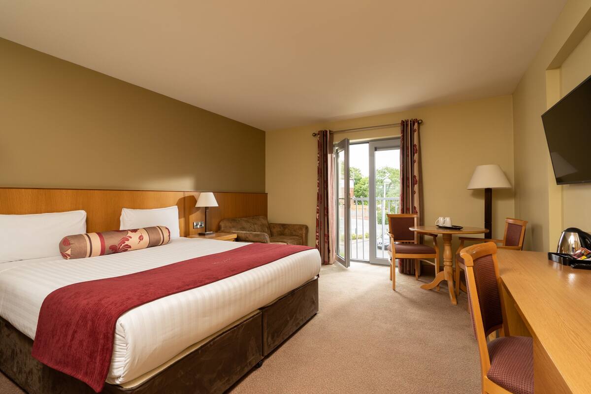 Ein Hotelzimmer mit einem großen Bett, einem Schreibtisch, einem Stuhl, einem Fernseher und einer Schiebetür zur Terrasse.