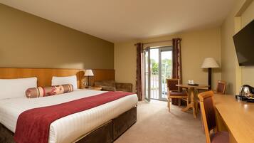 A hotel room with a large bed, a desk, a chair, a television, and a sliding glass door to the outside.