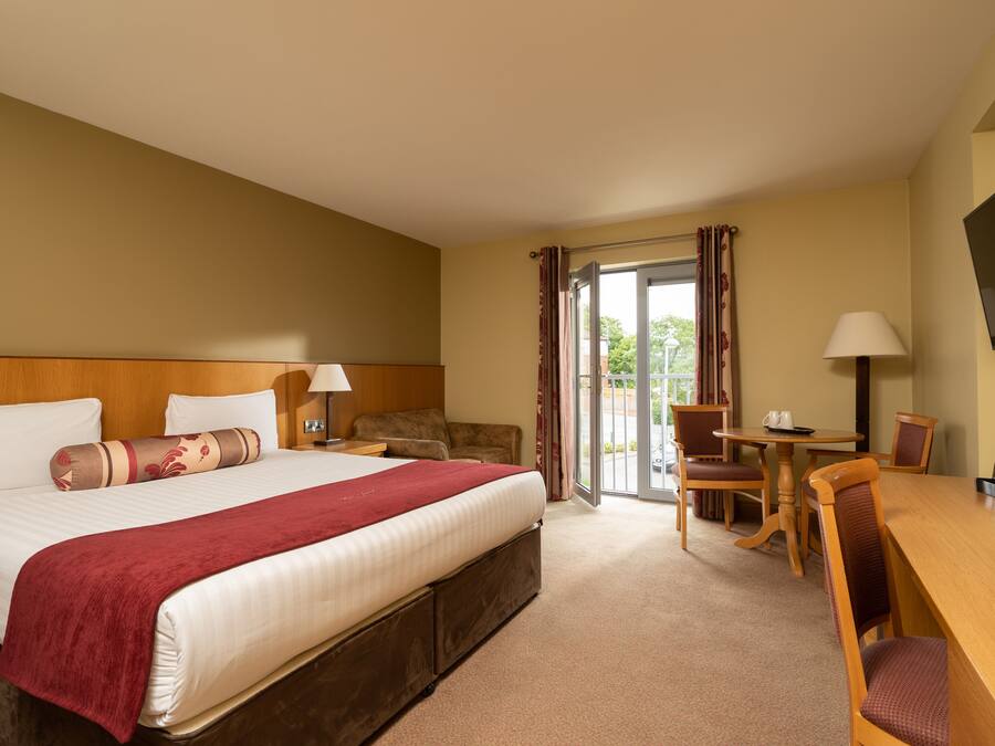 A hotel room with a large bed, a desk, a chair, a television, and a sliding glass door to the outside.