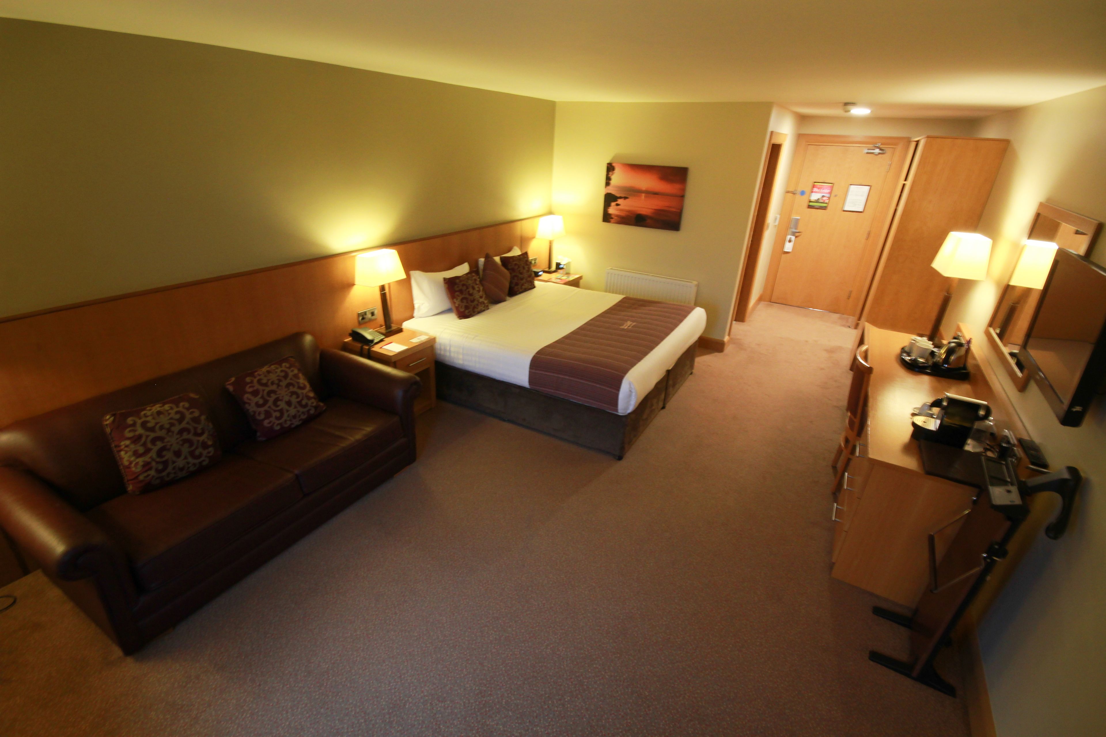 Una habitación de hotel con cama, sofá, escritorio y espejo.