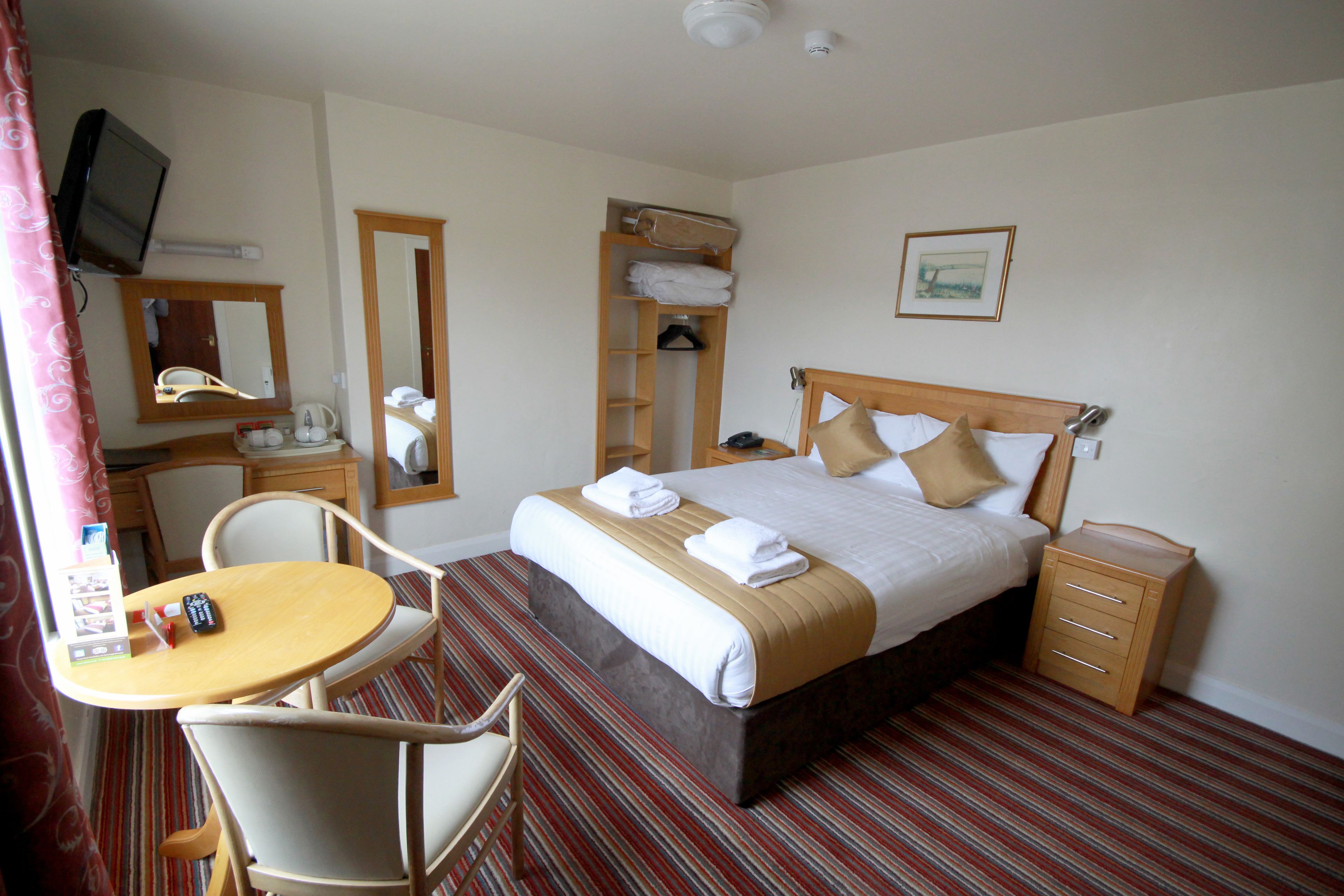 A hotel room with a bed, bedside table, chair, and a small desk with a chair.