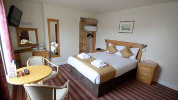 A hotel room with a bed, bedside table, chair, and a small desk with a chair.
