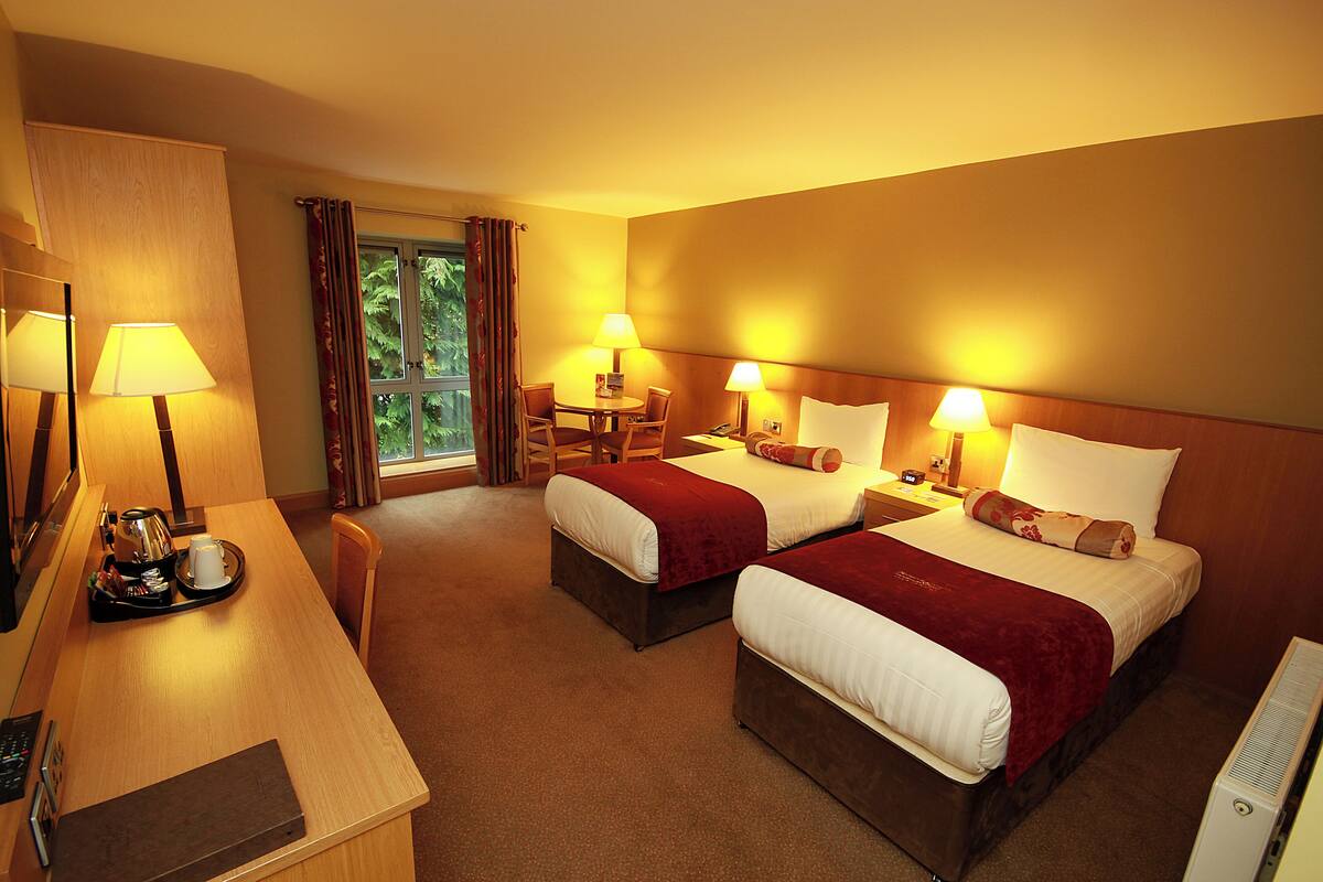 Ein Hotelzimmer mit zwei Betten, einem Schreibtisch mit Kaffeemaschine und einem Fenster mit Vorhängen.