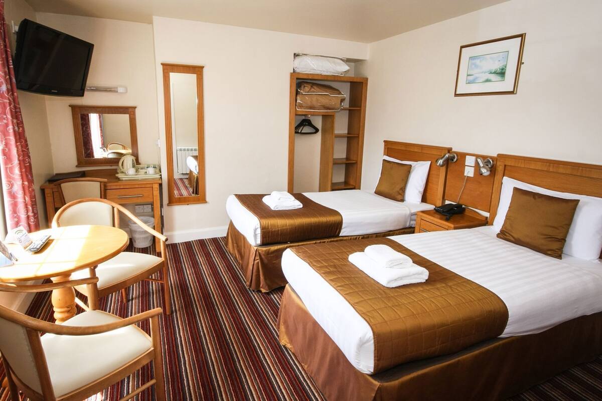 Ein Hotelzimmer mit zwei Betten, einem Schreibtisch, einem Stuhl, einem Fernseher, einem Spiegel und einem Bild an der Wand.