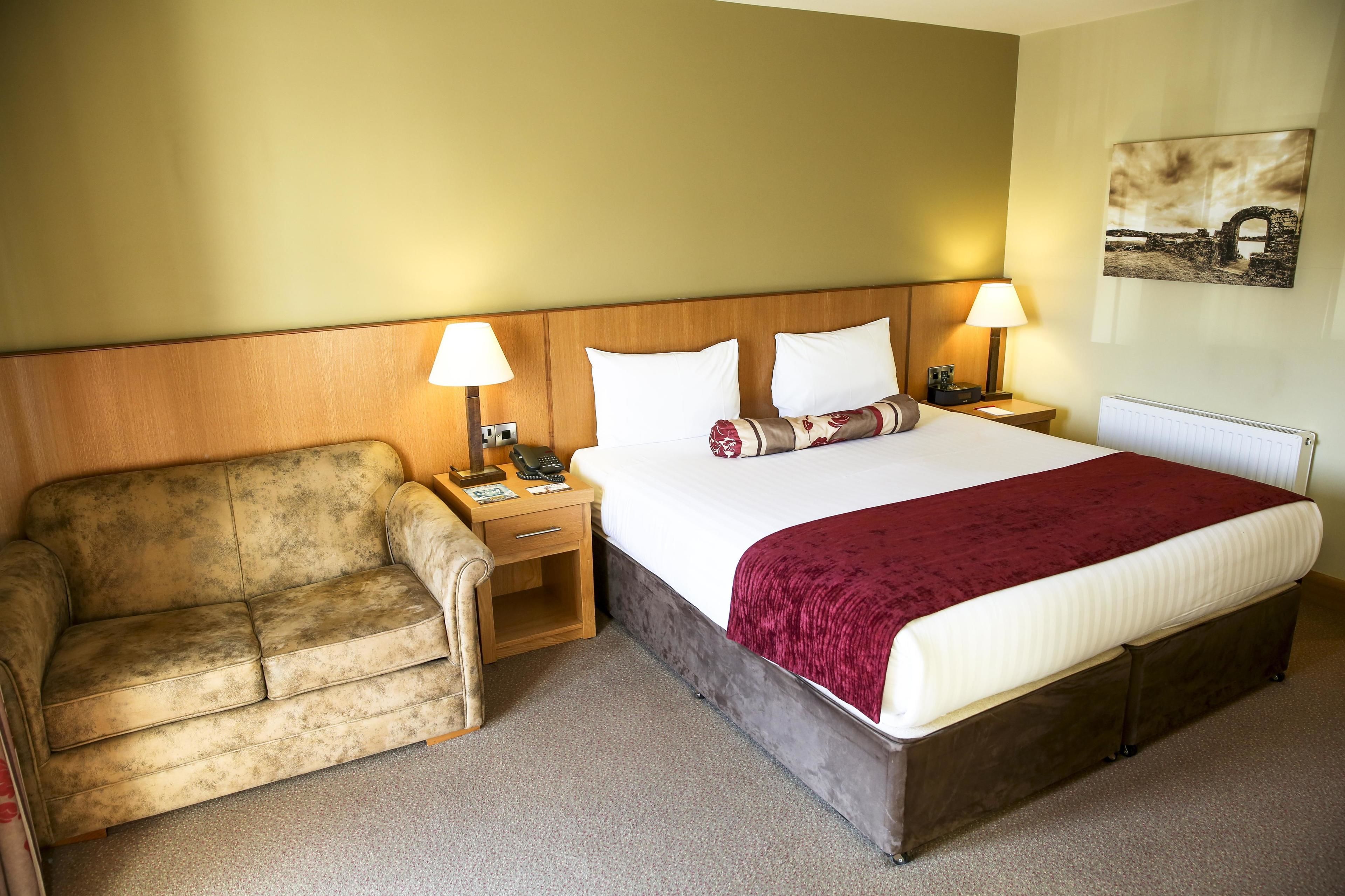 A hotel room with a bed, two bedside tables with lamps, a sofa, and a wall-mounted picture.