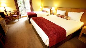 A hotel room with two beds, a desk, chairs, and a window with curtains.
