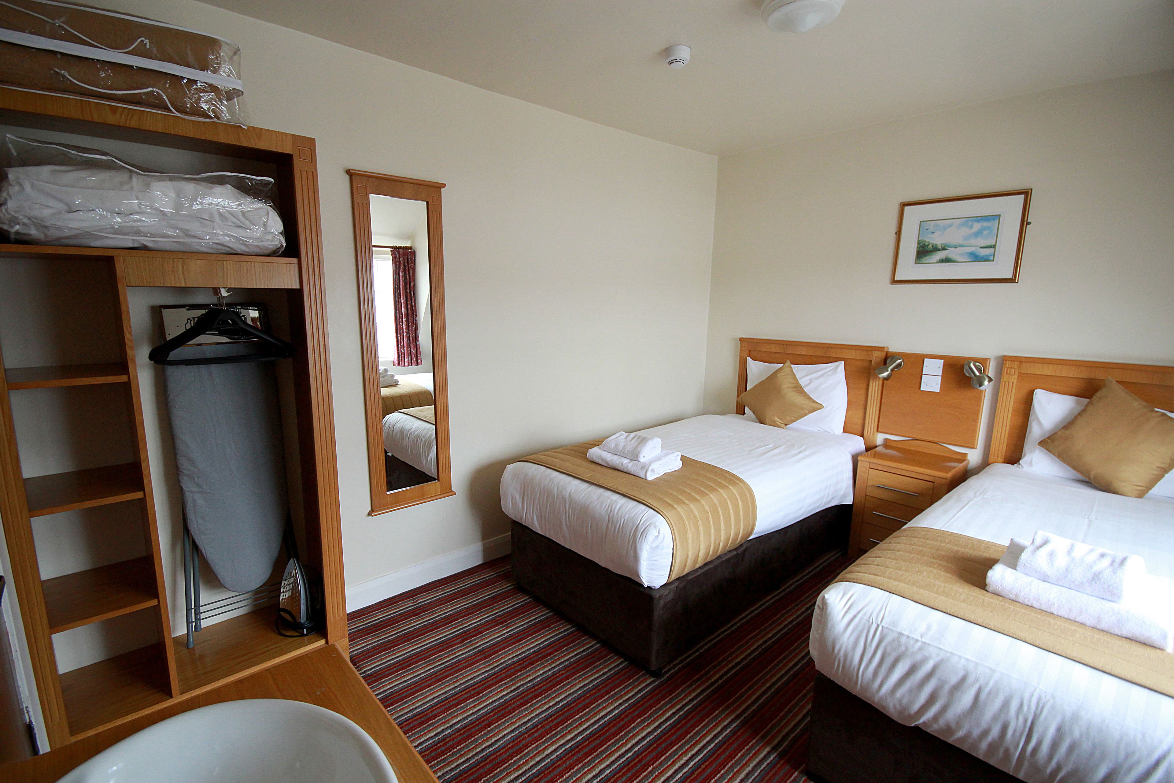 A hotel room with two beds, a wooden wardrobe, a mirror, and a framed picture on the wall.