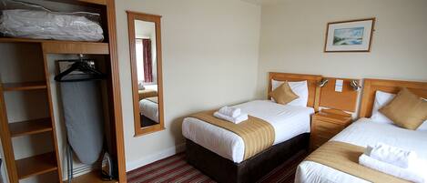 A hotel room with two beds, a wooden wardrobe, a mirror, and a framed picture on the wall.