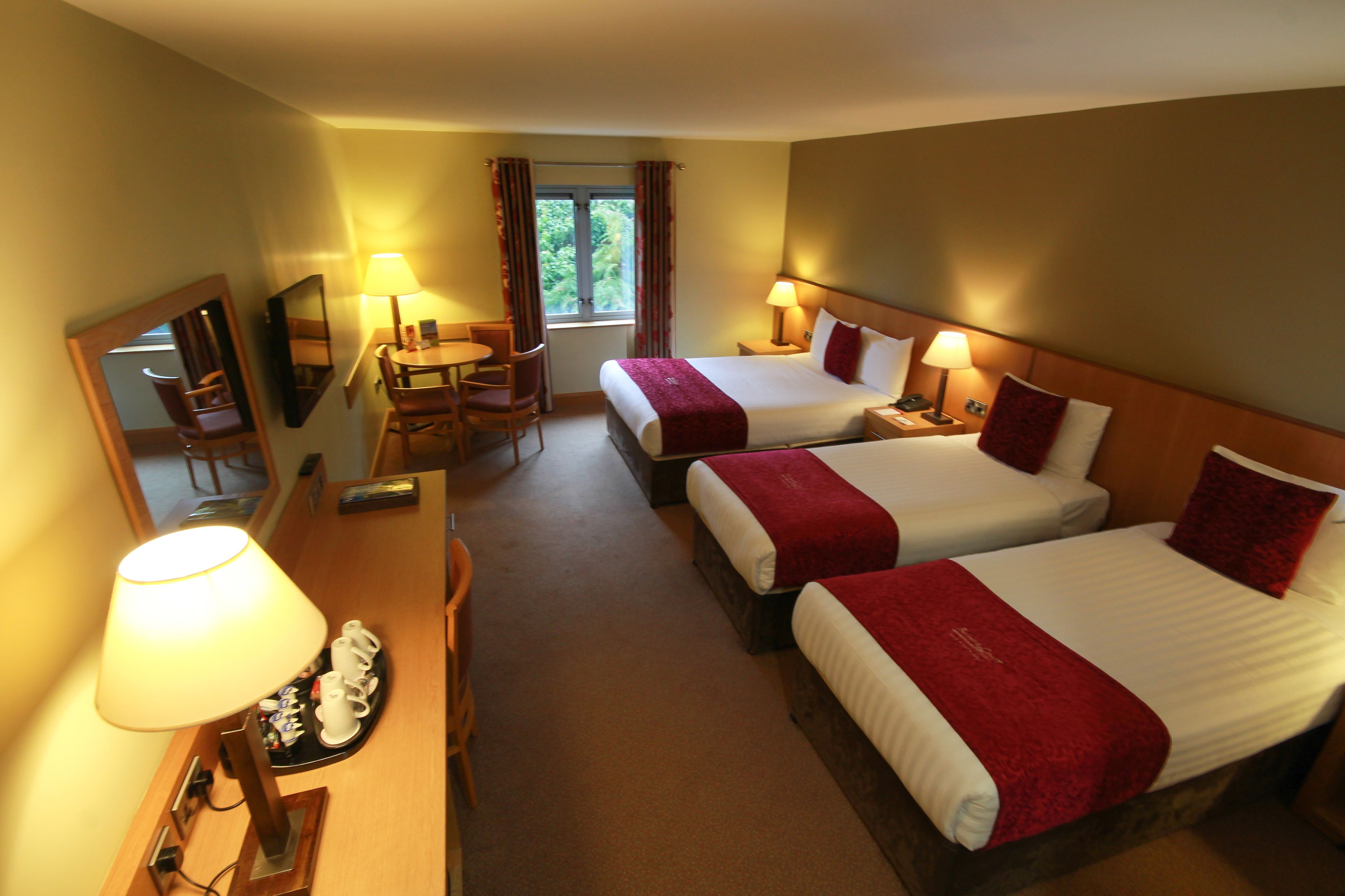 A hotel room with two beds, a desk, a chair, a TV, and a window with curtains.