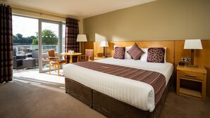 A hotel room with a large bed, two bedside tables, a small desk with a chair, a balcony with a table and chairs, and a view of greenery outside. - Belmore Court & Motel (Enniskillen)