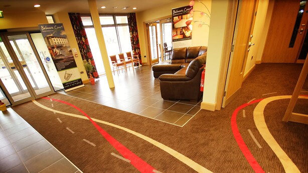 A hotel lobby with a carpeted floor, a seating area with a sofa, and a sign for Belmore Court. - Belmore Court & Motel (Enniskillen)