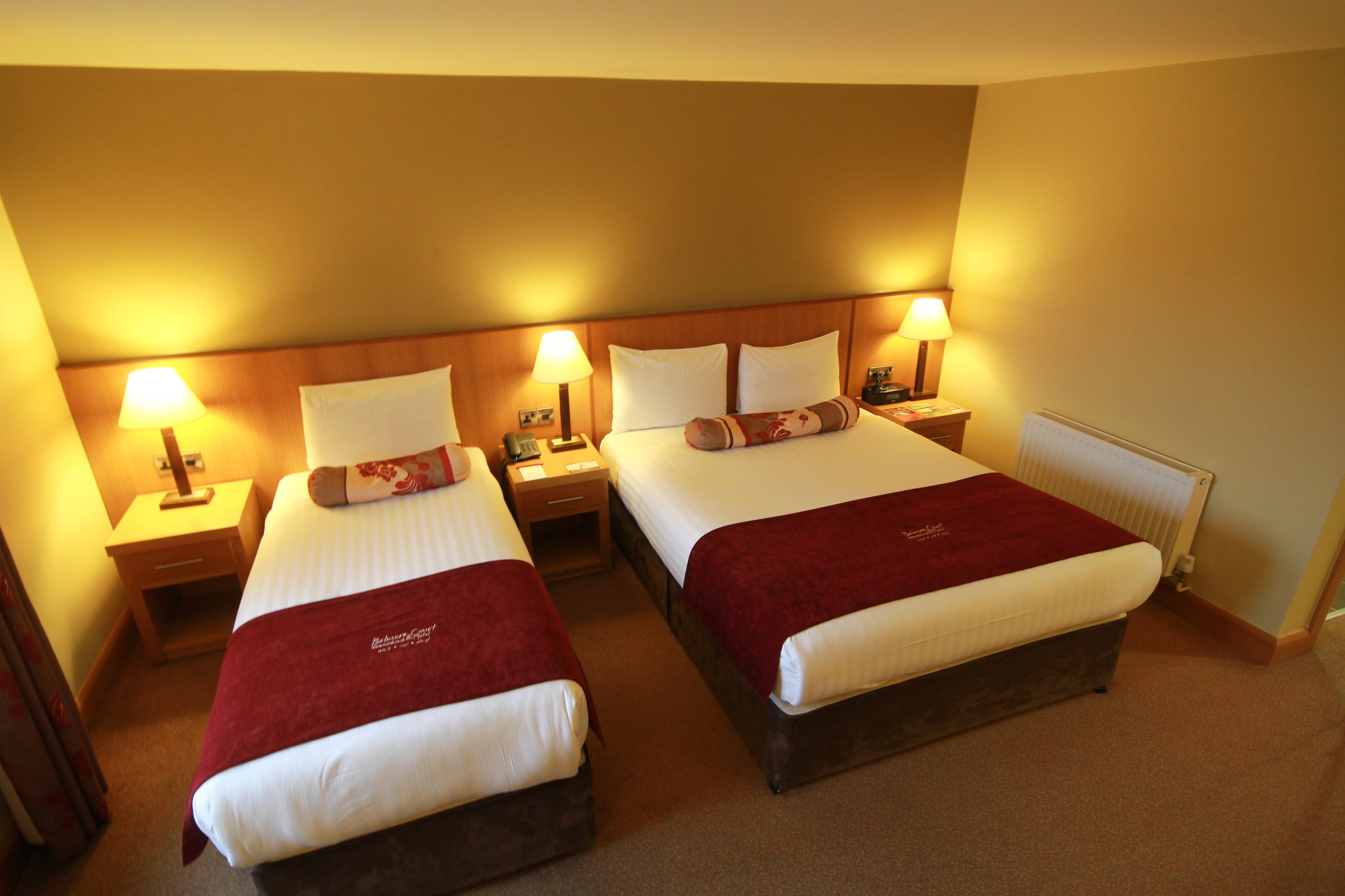Une chambre d’hôtel avec deux lits, chacun recouvert d’une couverture rouge, doté de draps blancs et agrémenté de lampes de chevet.