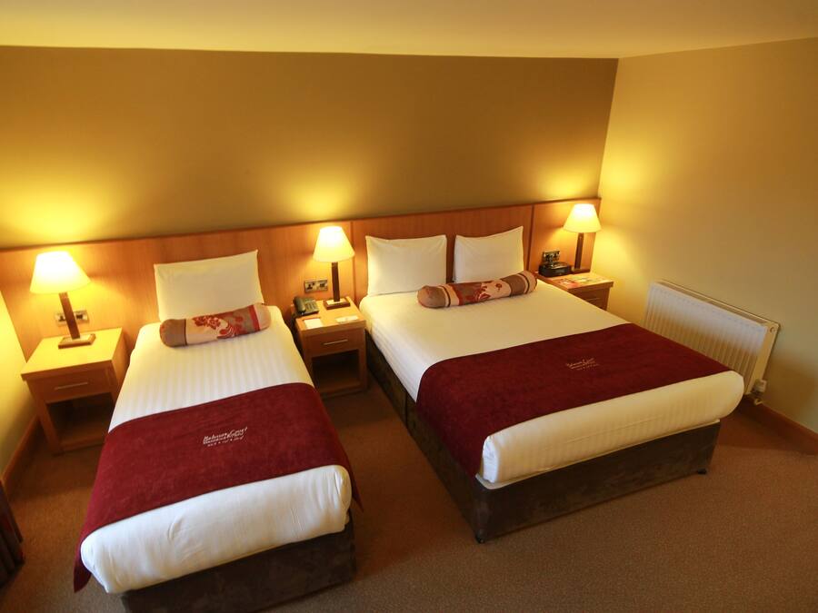 A hotel room with two beds, each with a red blanket, white linens, and bedside lamps.