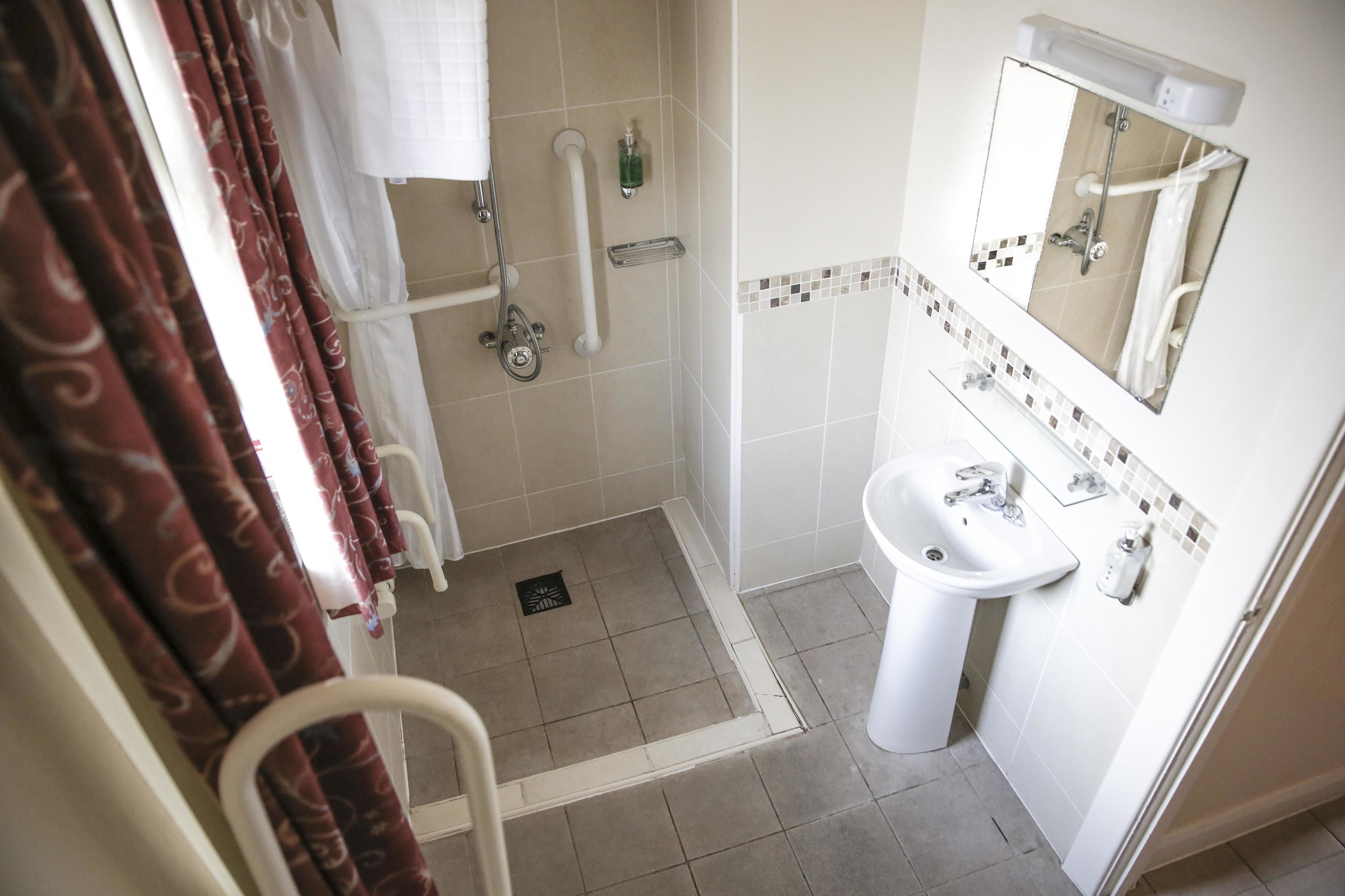 A bathroom with a shower, grab bars, a sink, and a mirror.