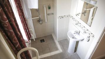Un bagno con doccia, maniglioni, lavandino e specchio.