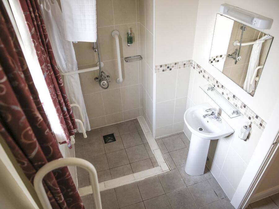 Un bagno con doccia, maniglioni, lavandino e specchio.