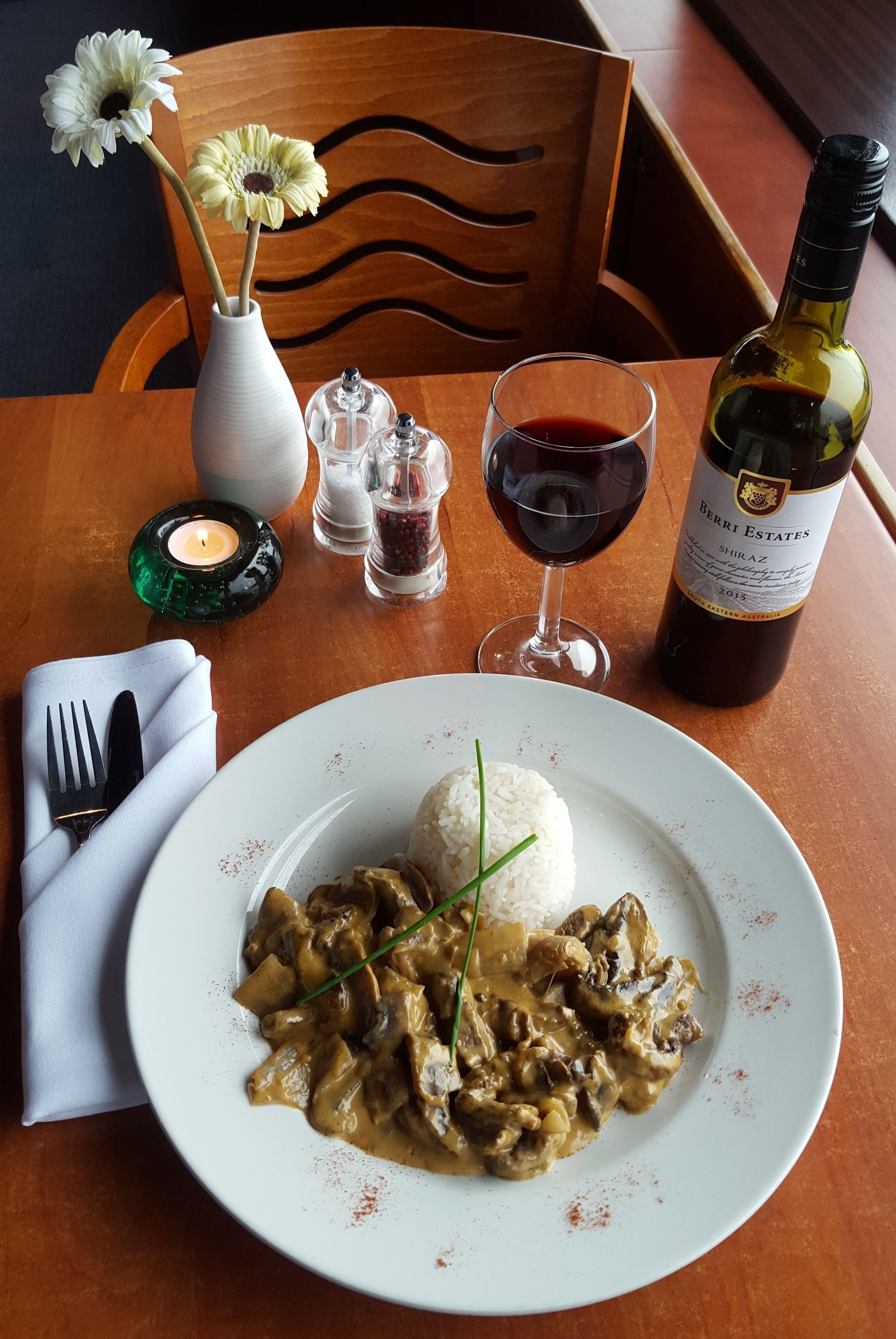 A dining table with a plate of mushroom risotto, a bottle of wine, and a vase with flowers.